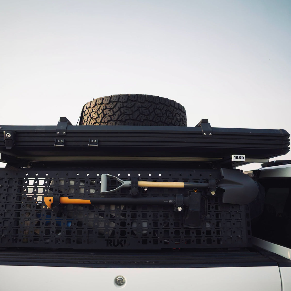 Shovel and axe clamped to a TRUKD V2 18.5" Accessory Panel on a TRUKD bed rack, with a rooftop tent and spare tire above